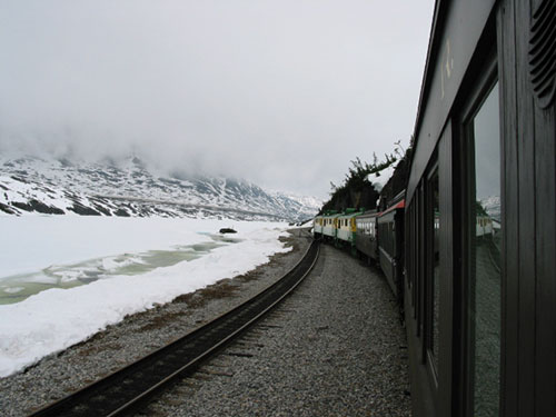 Train passes stream in snow along tracks