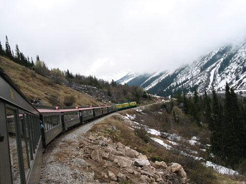 Many train cars viewable as train passes through mountains
