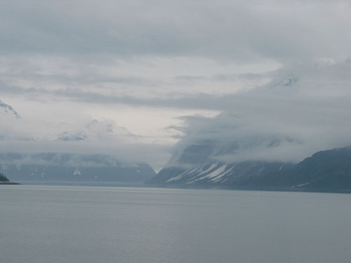 Fog surround the mountains with water in the foreground