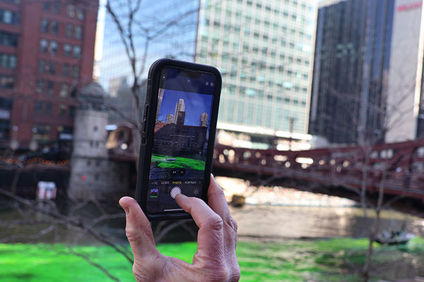 Person takes picture with phone of dyeing the Chicago River green