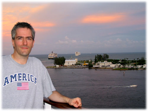 Pat stands on deck while two ships ext port in background