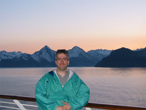 Pat standing at ship railing with sunset and water in background