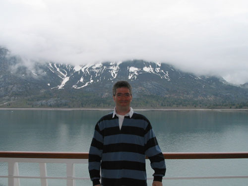 Pat stands along railing with water and mountains in the background