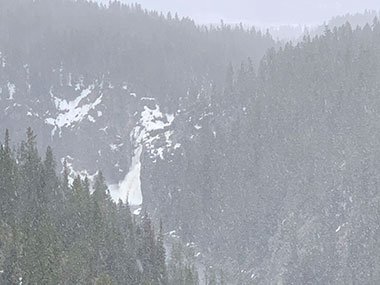 snow falls in Yellowstone National Park with waterfall in distance