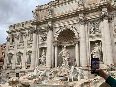 Camera an arm of person taking picture of Trevi Fountain