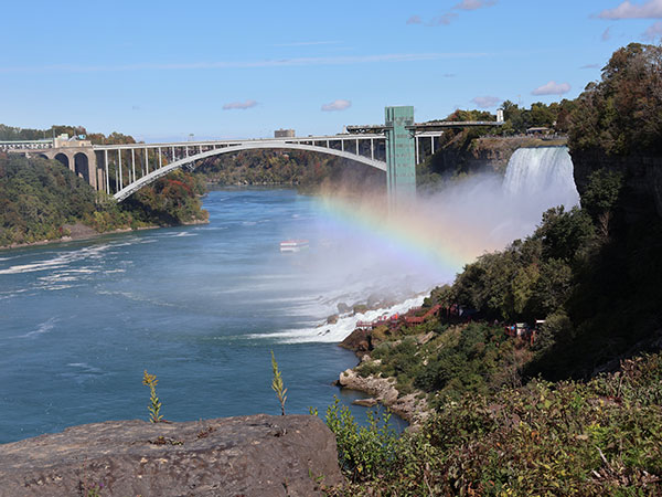 Rainbow near waterfall with bridge in distance
