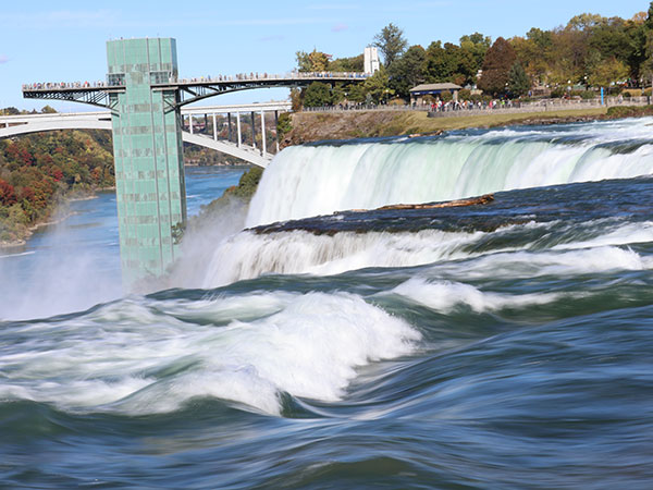 Close up of water flowing over Niagara Falls on American side with observation tower in background
