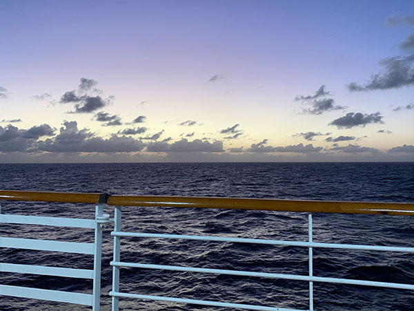 railing of ship with sunset beyond